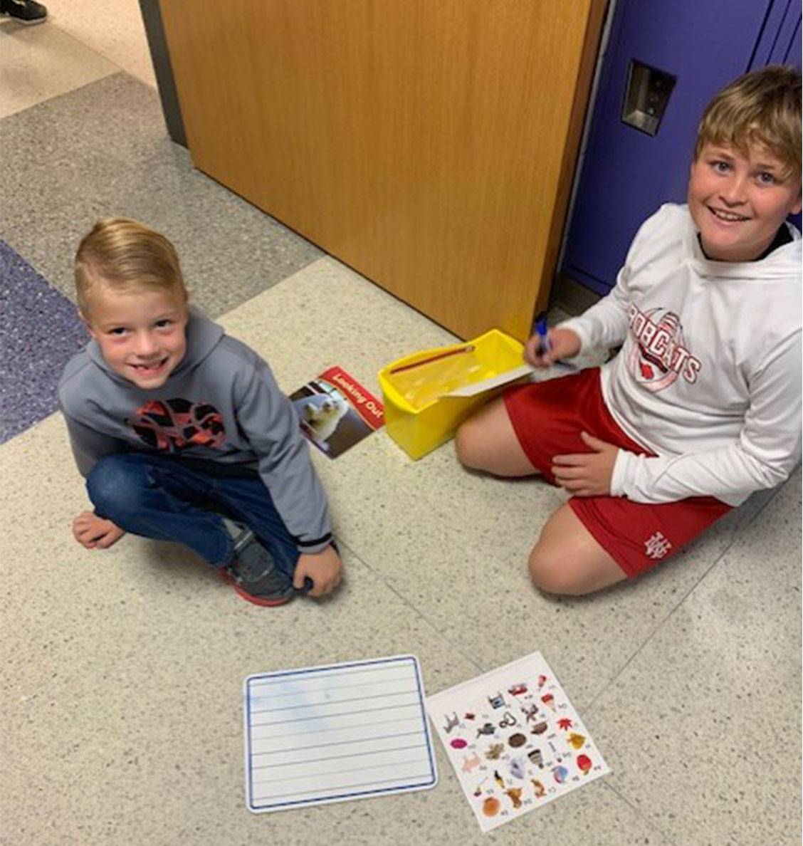 PES - 5th grade boy working with 1st grade boy during writing center in hallway