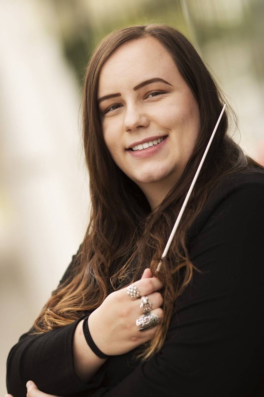 Macy Schmidt smiling and holding a conducting baton